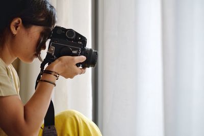 Side view of woman photographing with camera at home