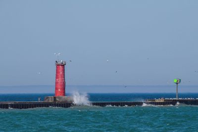 Lighthouse by sea against clear sky