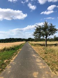 Empty road amidst field against sky