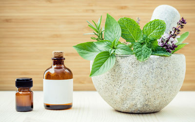 Close-up of herbs with mortar and pestle by bottles on table