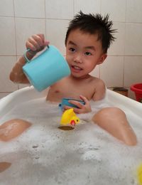 Shirtless boy playing with toys in bathtub at home