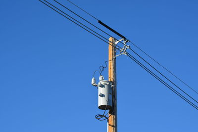 Low angle view of telephone pole against clear blue sky