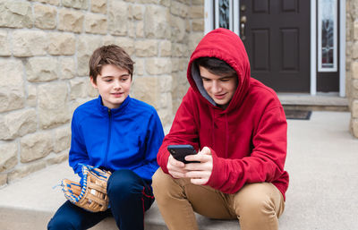 Two teenage boys sitting and talking on the front steps of a house.