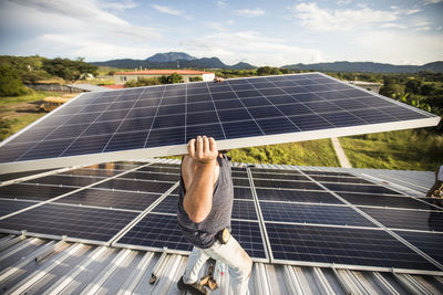 Strong construction worker carries solar panel above head on roof.