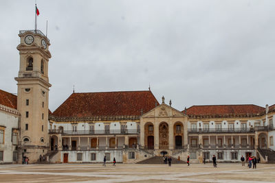 Group of people in front of historic coimbra university building against sky