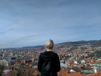 Rear view of woman looking at cityscape against blue sky