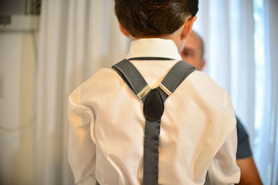 Rear view of boy wearing suspenders with father at home