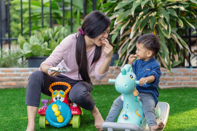 Mother and son eating food while sitting toys at park