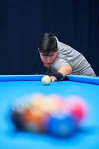 Serious boy in casual wear with cue stick preparing to hit ball while playing pool game at blue billiard table