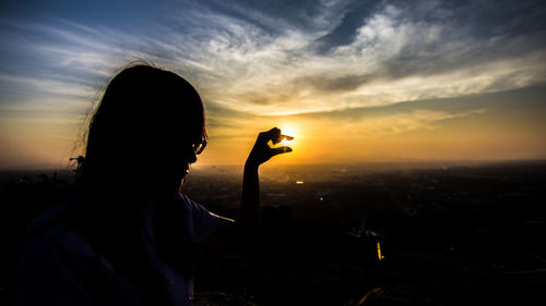 Optical illusion of woman holding sun against sky during sunset