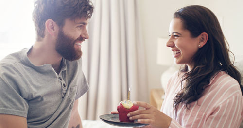 Happy woman with cupcake by man on birthday in bedroom