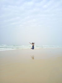 Happy young woman jumping at beach against sky