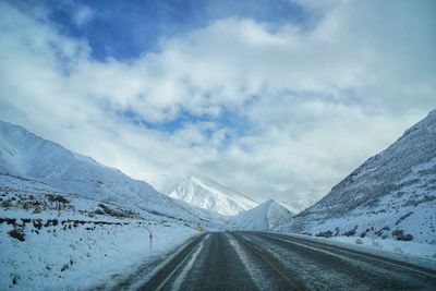 Road leading towards snowcapped mountains against sky