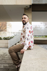 Portrait of a beaded man sitting on wall while looking camera