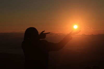 Silhouette woman gesturing by sea against sky during sunset