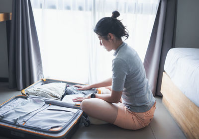 Young woman using mobile phone while sitting on bed at home