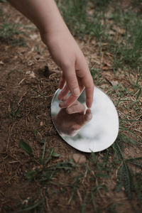 Cropped hand of woman touching mirror on ground