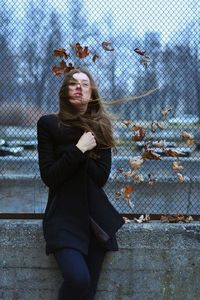 Portrait of young woman standing against fence