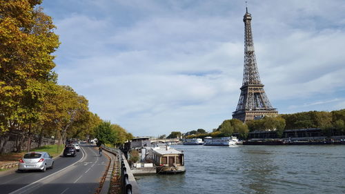 Cars moving on road by river against cloudy sky