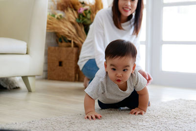 Mother looking at cute baby boy crawling on carpet