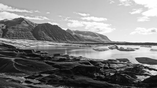 Rocky lakeshore by mountains against sky