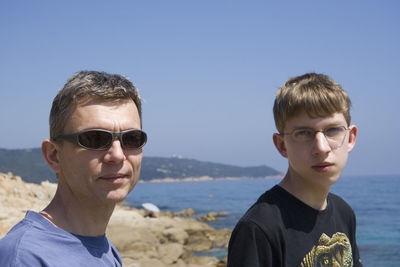 Portrait of father and son at beach against clear blue sky
