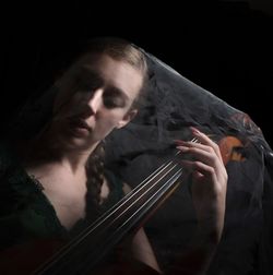 Young woman playing with violin standing against black background