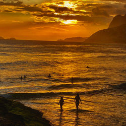 Silhouette people on sea against sky during sunset