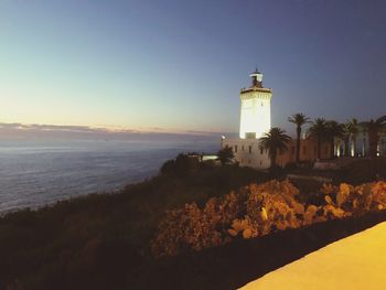 Lighthouse by sea against clear sky