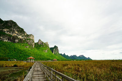 Walkway leading towards mountain against sky