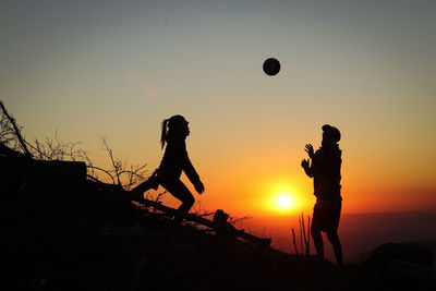 Silhouette people playing with ball against sky during sunset