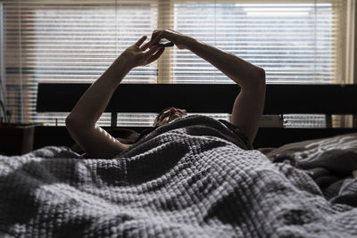Man using mobile phone while lying on bed at home