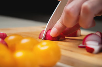 The fingers of a young woman cooking in the kitchen cut radishes and tomatoes, close-up