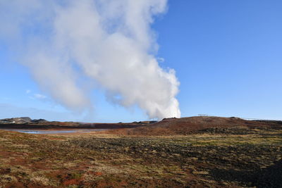 Smoke emitting from volcanic landscape against blue sky