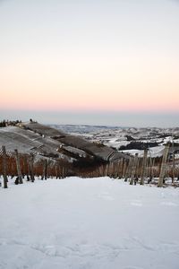 Snow covered landscape against sky during sunset