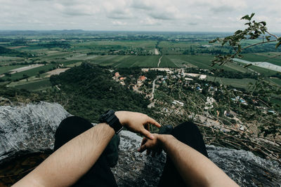 Low section of man sitting on rock against landscape