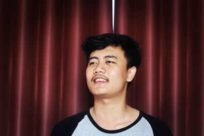 Close-up of smiling young man looking away against curtain