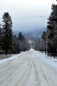 Snow covered road by trees against clear sky