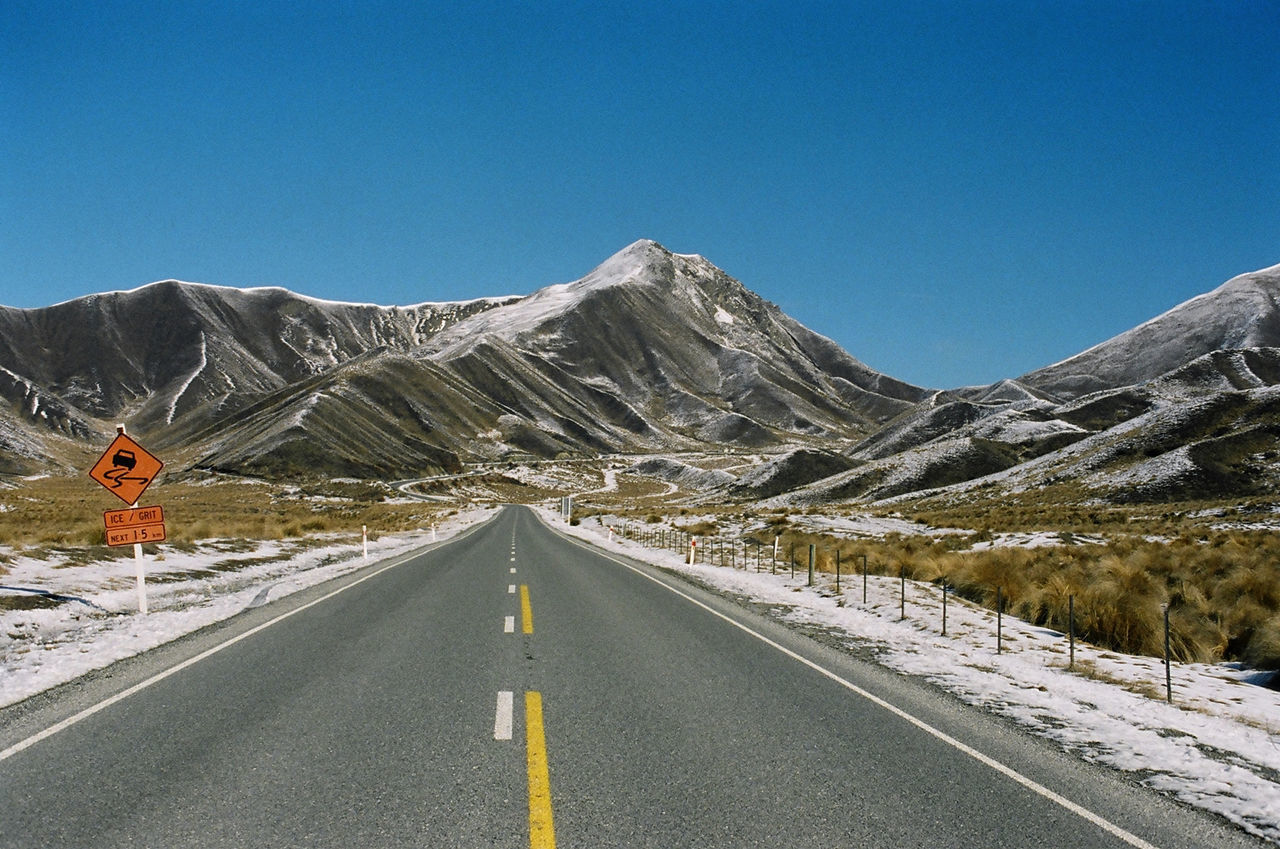 EMPTY ROAD ALONG SNOW COVERED MOUNTAIN AGAINST BLUE SKY