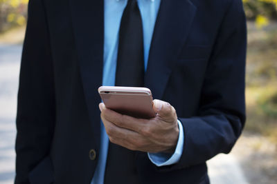 Midsection of businessman using mobile phone while standing outdoors