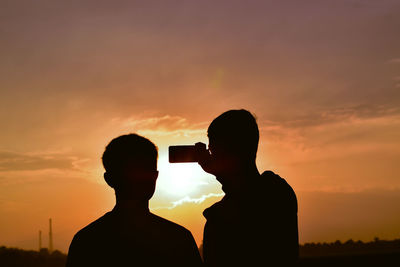 Silhouette people photographing against sky during sunset