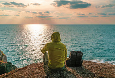 Rear view of man sitting on pier over sea against sky