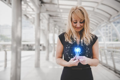 Digital composite image of woman holding illuminated electric bulb with icon