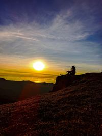Silhouette person on land against sky during sunset