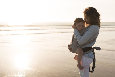 Mother carrying son while standing at beach