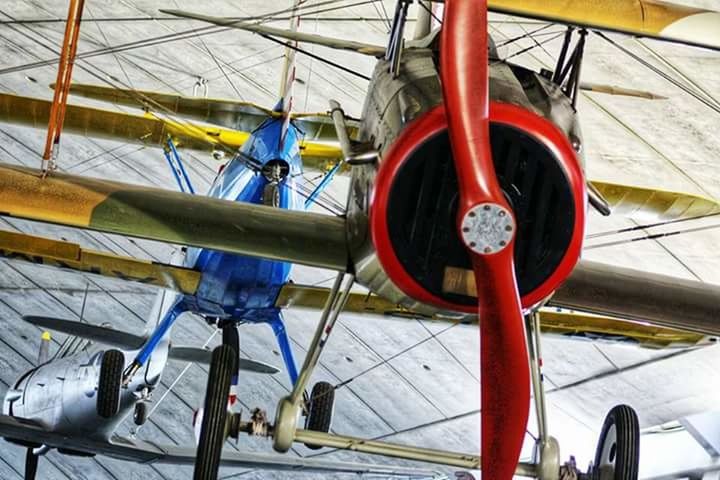 transportation, red, mode of transportation, air vehicle, airplane, industry, aerospace industry, day, indoors, metal, airplane hangar, low angle view, machinery, architecture, travel, engineering, built structure, incidental people, ceiling, wheel