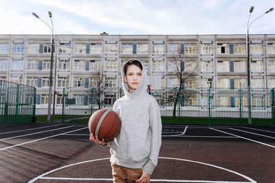 Portrait of teenager with basketball ball standing on court 
