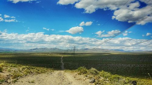 Dirt road on green landscape against sky