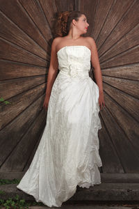 Full length of bride looking away while standing against wooden wall