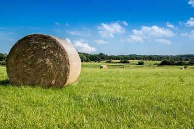 Hay bales on green field against sky